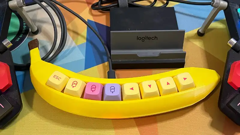 A bright yellow keyboard shaped like a banana with yellow, pink, and purple keycaps