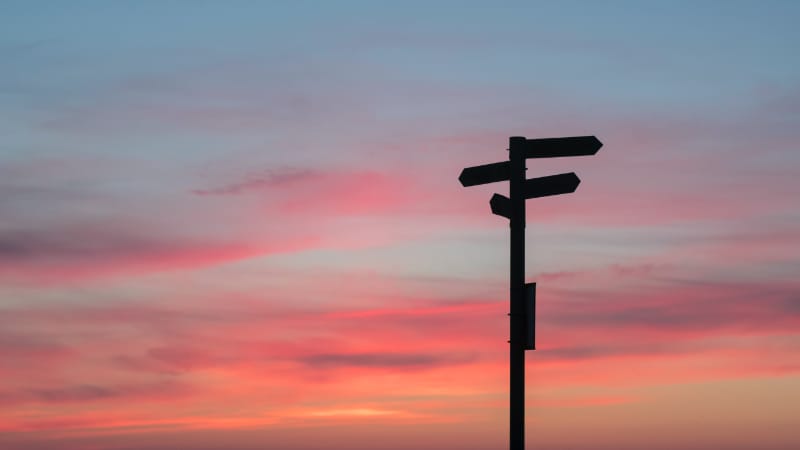 Signpost silhouette against sunset sky